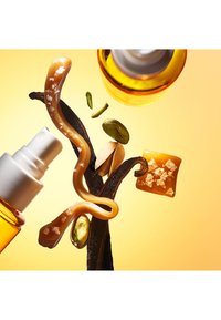 Botella pulverizadora con vainas de vainilla, cuadrados de caramelo espolvoreados con sal y pistachos sobre un fondo amarillo.