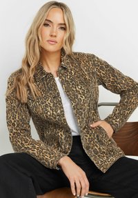 Leopardmönstrad denimjacka med knäppning, två bröstfickor och en figursydd design. Texturerat tyg i bruna och svarta nyanser.