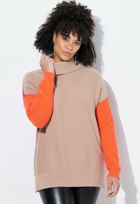 Maglione beige a maglia con colletto alto e maniche lunghe. Una manica è arancione e il design presenta uno spacco laterale all'orlo.