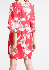 Robe fleurie rouge à manches courtes, ornée de grandes fleurs roses et vertes, en tissu doux, de forme évasée et avec un détail d'ouverture dans le dos.