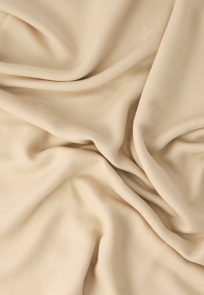 Μαλακό μπεζ ύφασμα με διακριτικά υφαντά σχέδια σε απαλές πτυχώσεις και καμπύλες, που αναδεικνύουν την υφή και τις απαλά φωτισμένες σκιές.