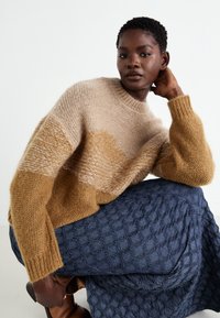 Stickad tröja med beige och senapsgula ränder, med en texturerad yta. Matchas med en blå vadderad kjol med en diamantmönster.