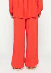 Losse, felrode outfit met een lange mouw top en wijde broekspijpen. Glad materiaal en eenvoudig ontwerp, minimaal detail.