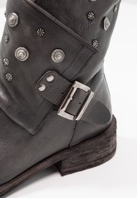 Czarne skórzane buty z srebrnymi ćwiekami i detalem w postaci klamry, z lekko zniszczoną teksturowaną podeszwą oraz zaokrąglonym noskiem.