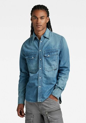 Denimskjorte i mellemblå, med knaplukning, to brystlommer og spidse krave. Blød tekstur med en afslappet pasform.