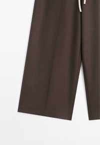 Hnědé široké kalhoty s hladkou texturou, vybavené stahovacím pasem a jemnými sklady pro střih na míru.