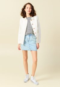 Witte denimjas met knopen, zwart-wit gestreept shirt, lichtblauwe denimrok en witte high-top sneakers. Neutrale achtergrond.