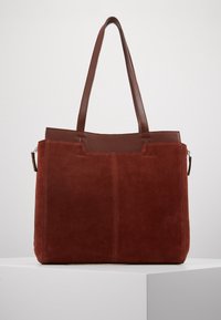 Sac fourre-tout en daim rouge avec des accents en cuir marron, doté de deux longues poignées, d'une poche zippée sur le côté et d'une forme rectangulaire élégante.