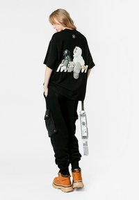 Camiseta negra con un diseño gráfico en la parte posterior, combinada con pantalones de chándal negros con bolsillos laterales y botas naranjas con suela gruesa.