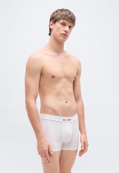 Boxer en coton blanc avec une taille élastique à logo coloré, coupe ajustée et texture lisse, présenté sur un modèle torse nu.