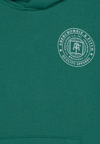 Zelená mikina s kapucí, která má kulatý bílý logo s textem "Abercrombie & Fitch" a "Quality Apparel". Vyrobena z texturované tkaniny s kapucí na šňůrku.
