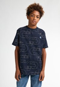 Camiseta de algodón azul marino con patrones geométricos blancos y cuello redondo. Mangas cortas, corte relajado y un pequeño detalle de logo en el pecho.