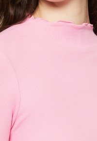 Ljust rosa ribbad topp med rundad, scalloped halsringning. Tyget har en mjuk textur och en figurnära design.