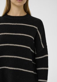 Suéter a rayas negro y crema con cuello redondo, corte holgado y textura suave. Presenta rayas horizontales en contraste y costuras de hombro caídas.