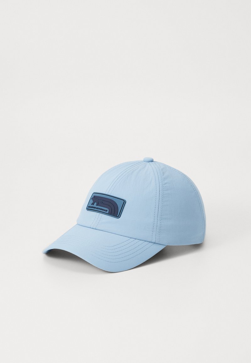 Casquette bleu clair avec une couronne structurée et une visière courbée. Présente une emblème en patch bleu foncé à l'avant. Fabriquée en tissu lisse et léger.
