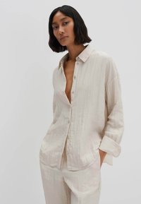 Camicia button-up oversize beige chiaro in un tessuto texture. Presenta un colletto e tasche sul petto, abbinata a pantaloni coordinati.