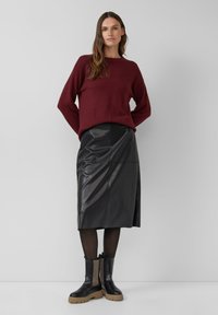 Bordeaux trui met een ribbelboord, gecombineerd met een zwarte leren midi-rok met een gladde textuur en diagonale naden. Zwarte enkellaarsjes.