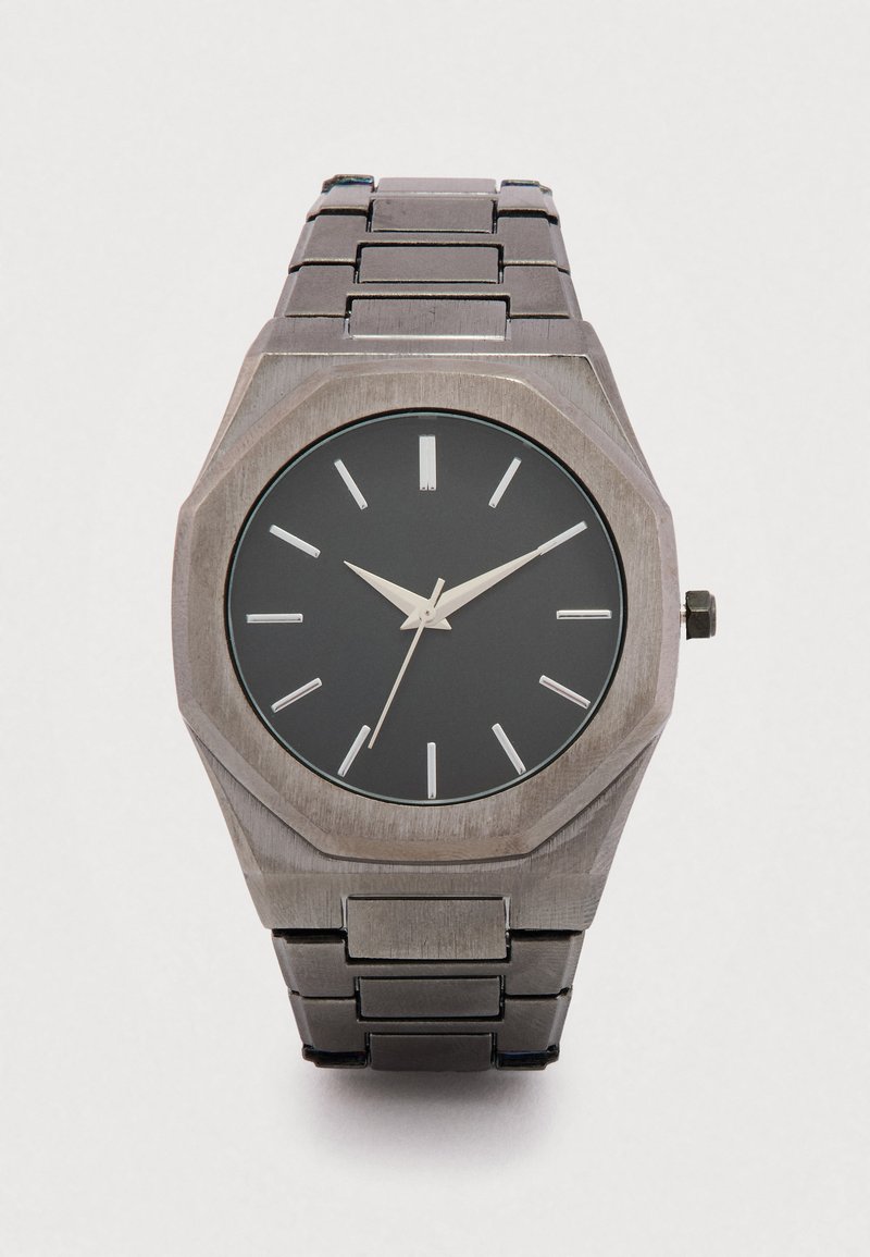 Achteckige Uhr mit einem gebürsteten silbernen Edelstahlarmband, schwarzem Zifferblatt, weißen Stundenmarkierungen und einem einfachen, minimalistischen Design.