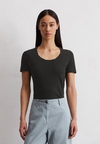 T-shirt noir à manches courtes avec un col rond, texture douce, associé à un pantalon bleu clair avec une fermeture à bouton et une coupe droite.
