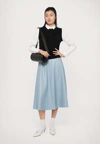 Gilet nero lavorato a maglia con decorazioni floreali, camicia bianca con colletto, gonna azzurra chiara, borsa cilindrica nera, calze bianche e mocassini a punta.