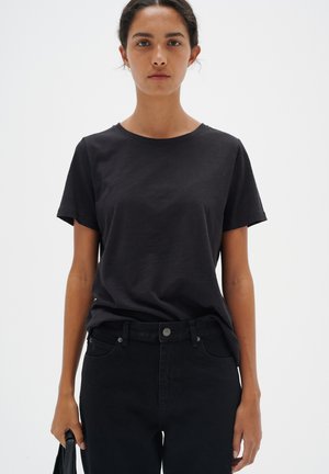 T-shirt en coton noir à manches courtes et col rond, assortie à un jean noir. Design simple, texture lisse, sans motifs visibles.
