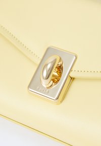 Borsa a tracolla gialla in pelle con un design elegante, dotata di una chiusura in metallo con finitura dorata e una texture liscia. Logo Furla impresso sull'hardware.