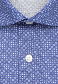 Chemise bleue à motifs géométriques blancs petits, col évasé et bouton blanc à quatre trous central fermé.