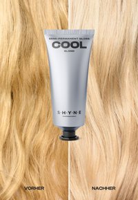 Półtrwały połysk do włosów w srebrnej tubce oznaczonej "Cool Blond" stoi pomiędzy dwoma pasmami falowanych, blond włosów, ukazując różnicę w kolorze.