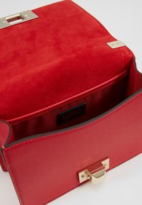 Rød håndtaske med en tekstureret suede klap og glat læderkrop. Guld hardware-lås og indvendig stribet foring. Brandlabel synligt.