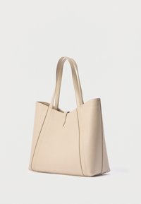 Μπεζ δερμάτινη τσάντα ώμου με διπλούς ιμάντες και μικρό κλείσιμο με ταμπ, τοποθετημένη σε απλό λευκό φόντο.