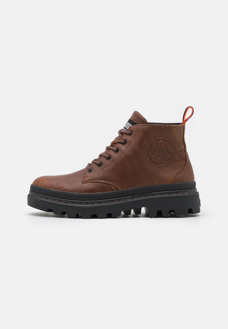 Bottines en cuir marron avec une semelle en caoutchouc noir épaisse, à bout rond et un design de laçage prononcé. Présente un logo et une languette rouge.