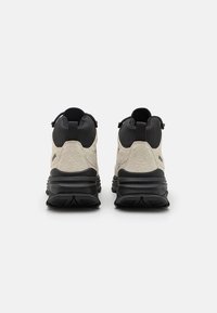 Cremefarbene und schwarze Wanderschuhe mit einer strukturierten Oberseite, robustem Gummi-Sohlen und Ziehschlaufen an der Ferse für einfaches Anziehen.
