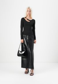 Schwarzes Langarmoberteil mit asymmetrischem Ausschnitt, kombiniert mit einem schwarzen Maxirock aus Leder. Accessoriert mit einer kleinen schwarzen Handtasche.
