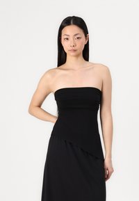 Svart strapless klänning med rynkad bodice och asymmetrisk fåll. Tillverkad av slätt tyg och har en elegant silhuett med minimal design.