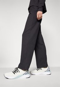 White athletic sneakers with a patterned heel and light blue accents, paired with loose-fitting, dark gray ribbed pants.