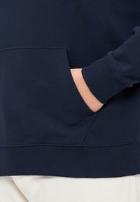 Felpa blu navy con tasca a marsupio, polsini e orlo a costine. Tessuto morbido con dettagli a cucitura piatta sui lati.