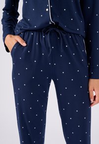 Ensemble de pyjama bleu marine avec motif d'étoiles blanches. Tissu doux, manches longues, haut à boutons, pantalon à taille élastique avec cordon de serrage ajustable et poches.