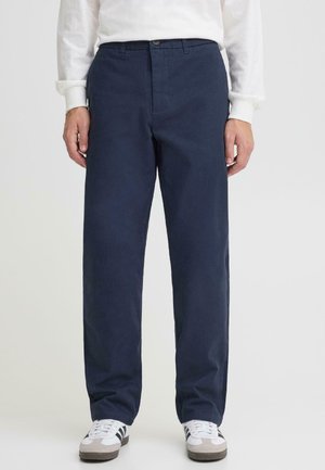 Marineblå bukser lavet af bomuld med et lige-ben design, der har knaplukning og sidelommer, kombineret med hvide sneakers.