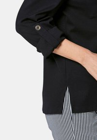 Zwarte stof top met een opklapbare manchet met een zilveren knop, zijsplitdetail, gecombineerd met wit en zwart geruit patroon ondergoed.