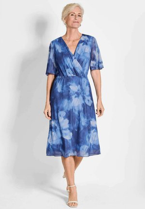 Robe enveloppante bleue à motifs floraux avec des manches courtes, longueur genoux et une texture douce et fluide. Présente un décolleté en V profond et une taille cintrée.