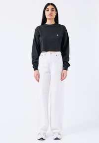 Sudadera negra corta con mangas largas, combinada con jeans blancos de pierna ancha de cintura alta, y zapatos deportivos blancos.