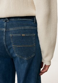 Tmavě modré džíny s úzkým střihem, s malou zadní kapsou s vyšitým "XX" a jemnými švy.