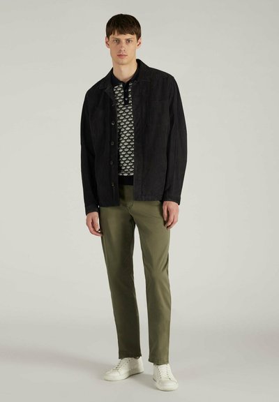 Schwarze Knopfjacke über einem gemusterten marineblauen Pullover, kombiniert mit olivgrünen Hosen und weißen Sneakers. Einfaches Design und Textur.