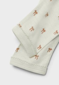 Chaussettes en coton blanches ornées de petits motifs de nœuds bruns répétés. Les bords supérieurs présentent une délicate bordure texturée.