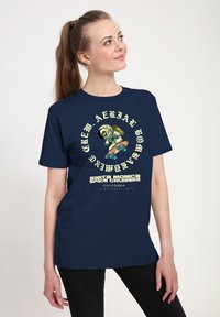 Námořnické tričko s předním grafikou kostlivce v skafandru, který jezdí na skateboardu, s textem uspořádaným do kruhu a kontrastními barvami.