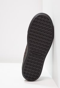 Semelle extérieure de chaussure en caoutchouc noir avec un motif étoile texturé, comprenant un détail de logo latéral. Matériau supérieur de ton neutre partiellement visible.