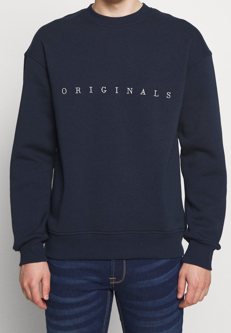 Sweatshirt in cotone blu navy con il testo "ORIGINALS" in bianco sul petto. Presenta un colletto a girocollo e polsini e fondo a costine.