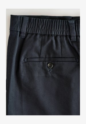 Sötét tengerészkék nadrág, rugalmas derékkal, övhurkokkal és egy hátsó zsebbel, amelyet egyetlen fekete gomb díszít. Simának tűnő anyag, enyhén fényes felülettel.