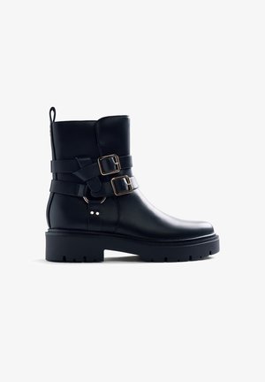 Bottes de cheville en cuir noir avec deux boucles décoratives, semelle texturée et talon épais. Caractéristiques d'une boucle à l'arrière pour un enfilage facile.