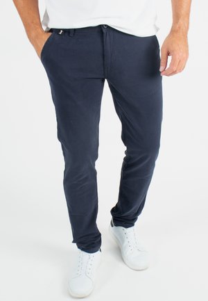 Pantalons slim bleu marine en tissu doux, dotés de poches avant et d'une fermeture à bouton, associés à des baskets blanches.